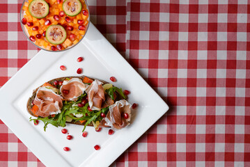 Italian appetizer bruschetta with roasted tomatoes, mozzarella cheese, garlic, herbs, prosciutto crudo and sauce.