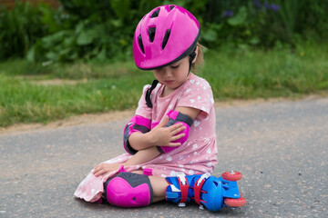 A little girl roller skating in full protection fell on the asphalt