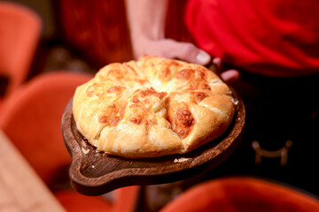Close up of waiter serving a plate of Khachapuri - hachapuri in Adjarian. Waiter at work. Restaurant service.