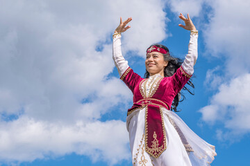 Fototapeta premium Young tender girl dancing national dance in a beautiful costume under the open blue summer sky