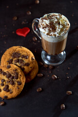 Close up of a glass cup of coffee with whipped cream and chocolate on it, chocolate chip cookies...