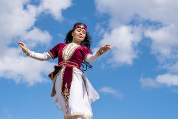 Fototapeta premium Young tender girl dancing national dance in a beautiful costume under the open blue summer sky