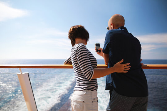 bald man and brunette woman traveling on cruise liner ship and taking pictures from smartphone on balcony 