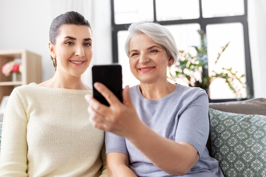 family, generation and people concept - happy smiling senior mother with adult daughter taking selfie by smartphone at home