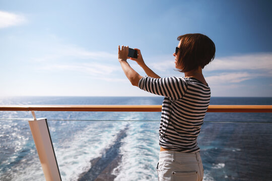 beauty adult brunette woman with hairstyle taking pictures with her smartphone from the deck on cruise liner ship.Travel concept.