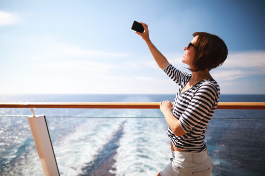beauty adult brunette woman with hairstyle taking pictures with her smartphone from the deck on cruise liner ship.Travel concept.