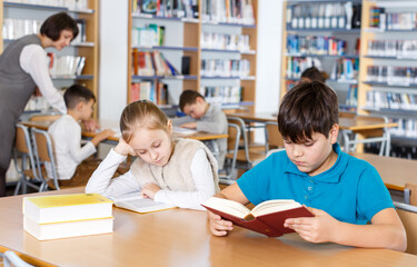Cute tween girl and intelligent boy studying together in school library, reading books