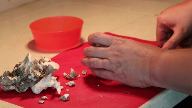 Hands breaking up a cluster of maitake mushrooms, then slicing on a red cutting board with a santoku chef knife and finally putting cut mushrooms into a bowl