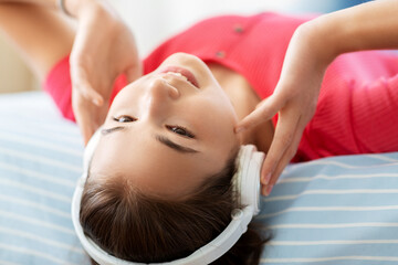 children and technology concept - portrait of smiling teenage girl in headphones lying on bed upside down and listening to music at home