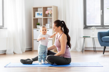Fototapeta na wymiar family, sport and motherhood concept - happy smiling mother with little baby sitting on exercise mat at home