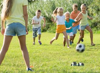 Obraz na płótnie Canvas team of energetic joyful children running with ball on meadow outdoors .