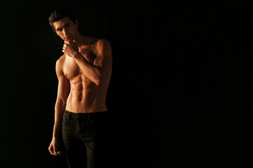 Strong athletic handsome young man with naked torso, showing his six abs on dark black background.