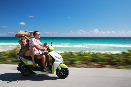 Beautiful young couple in love enjoying and having fun riding on a scooter near beach with beauty and clear water at sea - Powered by Adobe