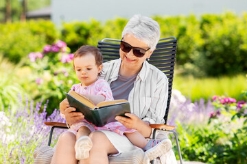 Fototapeta premium family, generation and people concept - happy grandmother with baby granddaughter reading book at summer garden