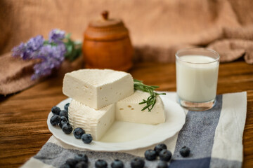 A glass of goat milk and a head of goat milk cheese stand on a wooden table. Cheese at home.