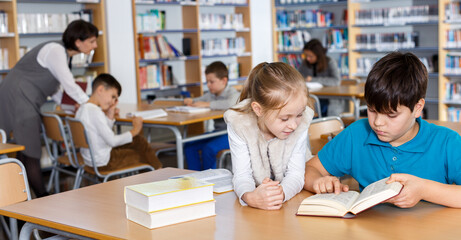 Portrait of two school children preparing for lesson in school library, reading textbooks together