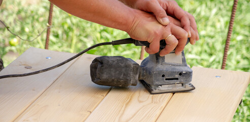 Woodworking tool. Work on a wooden kitchen table. Carpenter grinds the surface of furniture.