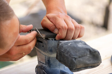 A carpenter replaces sandpaper on a woodworking tool.