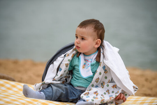 Portrait of a cute baby boy on the beach on a summer day wrapped up from the wind