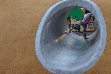 Bangkok, Thailand - Jul 25, 2020 : Asian little girl playing inside a tunnel in the park for children. Playground on background. Selective focus.