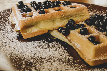 Belgian waffles with berries on a plate with powdered sugar.