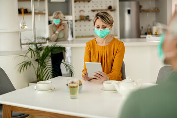 Woman with protective face mask using digital tablet at home.