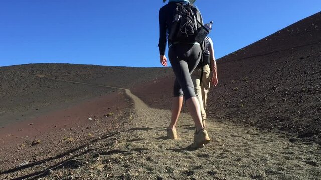 2 people hike through Haleakala sliding sands trail in Maui Hawaii. Hiking through dry barren volcanic ash terrain.  