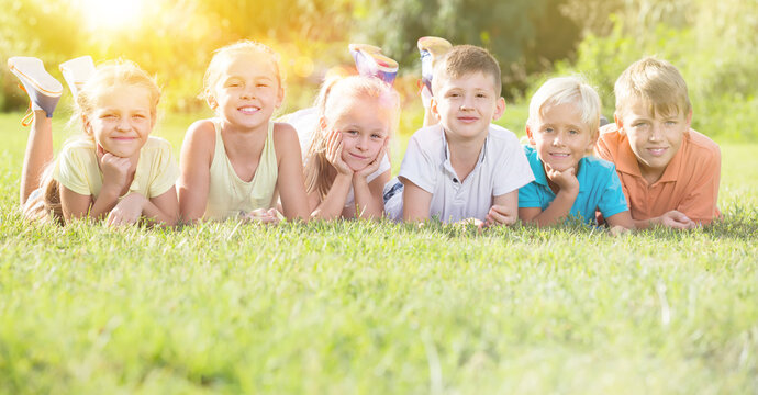 Group of smiling kids in elementary school age lying on green grass in park