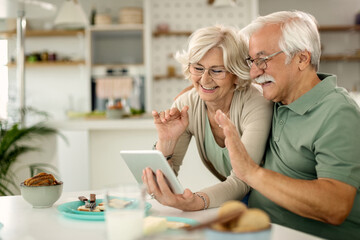 Happy senior couple waving while making video call over touchpad at home.