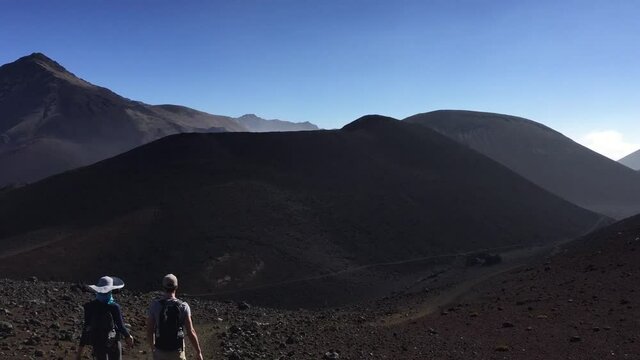 Hikers hike through Haleakala crater sliding sands trailer. Volcanic barren dry terrain. Maui Hawaii. 