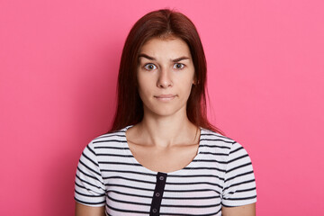 Fototapeta premium Misunderstanding lady looking directly at camera, wearing casual striped t shirt, posing isolated over pink background, looks at camera with serious look.