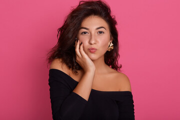 Lovely woman with gorgeous curly hair giving kiss and keeping hand on cheek, wearing black shirt...