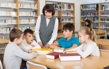 Group of school kids studying in school library with friendly female teacher..