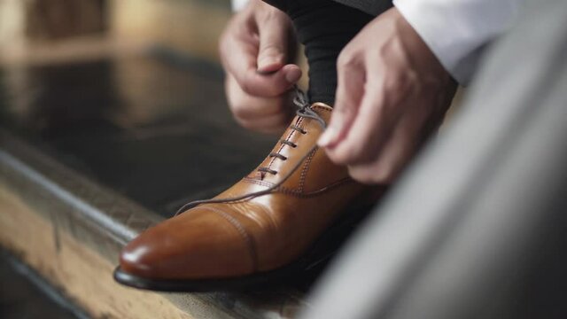 Man ties brown leather dress shoes before wedding ceremony. Close up of shoes and hands. Camera flash goes off. 