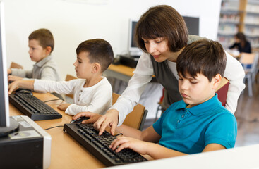 Friendly woman teacher helping tween boy during lesson in computer room of school library