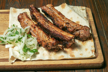 Spicy hot grilled spare ribs from a summer BBQ served with a hot chili pepper and fresh tomatoes on an old vintage wooden cutting board.