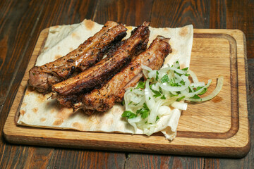 Spicy hot grilled spare ribs from a summer BBQ served with a hot chili pepper and fresh tomatoes on an old vintage wooden cutting board.