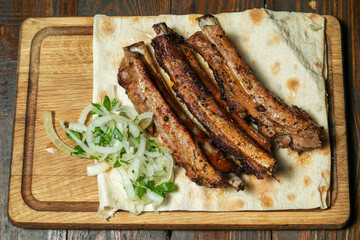 Spicy hot grilled spare ribs from a summer BBQ served with a hot chili pepper and fresh tomatoes on an old vintage wooden cutting board.