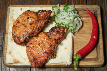 Spicy hot grilled spare ribs from a summer BBQ served with a hot chili pepper and fresh tomatoes on an old vintage wooden cutting board.