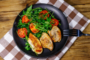 Fried chicken breast with salad of fresh arugula and cherry tomatoes on wooden table. Top view