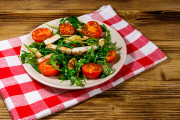 Tasty salad of fried chicken breast, fresh arugula and cherry tomatoes on wooden table