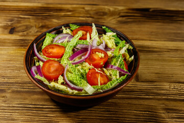 Healthy salad with savoy cabbage, cherry tomato, red onion and olive oil on wooden table