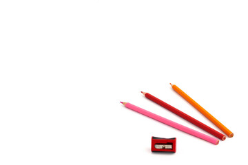Three colored pencils isolated on a white background, a red pencil sharpener nearby. Banner on the site, copy space.