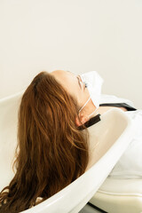 Young girl with long brown hair washing her head at the hairdresser's Social distancing. Use of the...