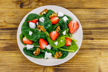 Fresh healthy salad with strawberry, spinach, walnuts and feta cheese on wooden table. Top view