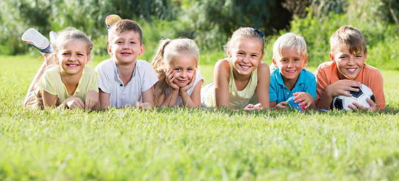 positive children lying on green grass on bright summer day