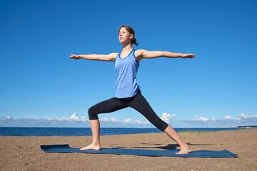 Fototapeta premium Young slim girl doing yoga on the beach on a sunny morning