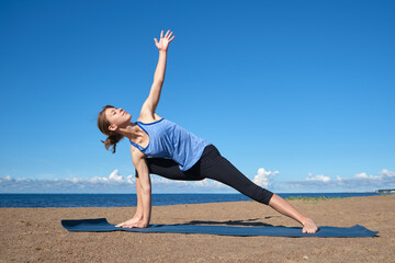 Young slim girl doing yoga on the beach on a sunny morning, stretching before doing sports