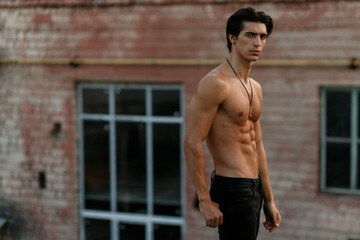 Horizontal view. Athlete strong young man shirtless in black jeans, posing with attitude on old...