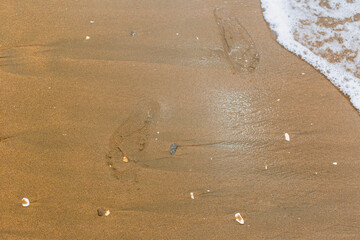 Footprints in the sand. Sandy beach with waves.